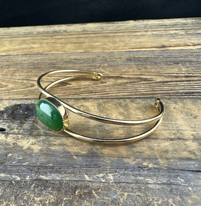 Gold cuff bracelet with a green jade cabochon in a beaded bezel, shown from the side
