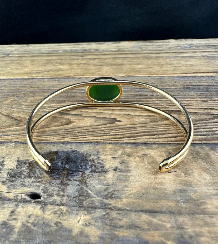 Open gold bracelet displaying the jade centerpiece from a low angle on a rustic wooden surface