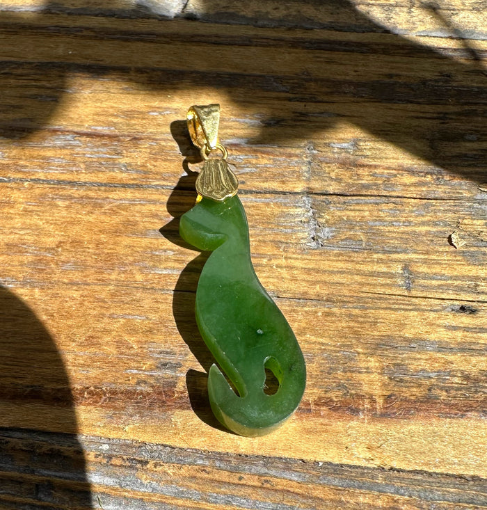 Green jade cat pendant with gold bail resting on a wooden surface