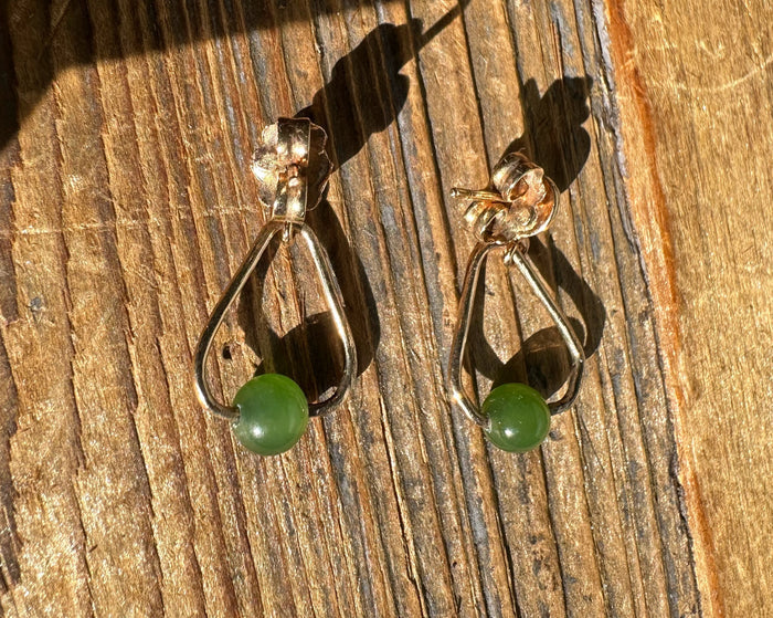 Pair of vintage jade triangle earrings with green beads and gold-tone teardrop frames on a wooden surface