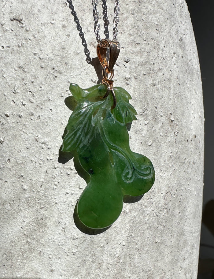 Jade gourd pendant on a chain with copper bail against a textured light stone background
