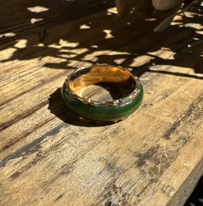 Top-down view of green jade ring with a gold-toned border resting on wood.