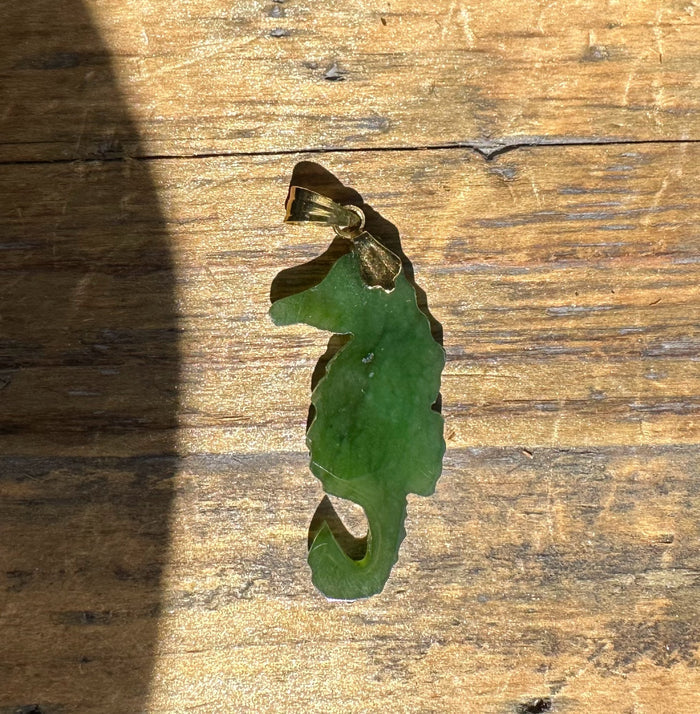 Green jade seahorse pendant with gold bail against a wooden background