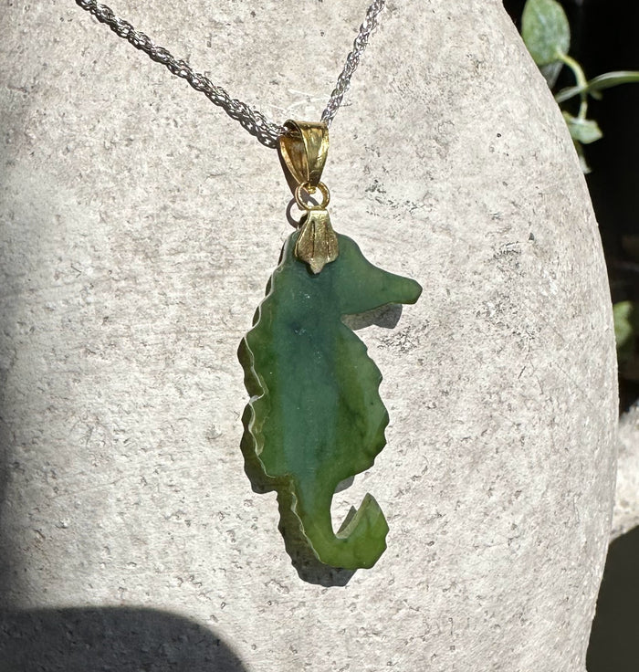 Green jade seahorse pendant with gold bail on a silver chain against a stone background