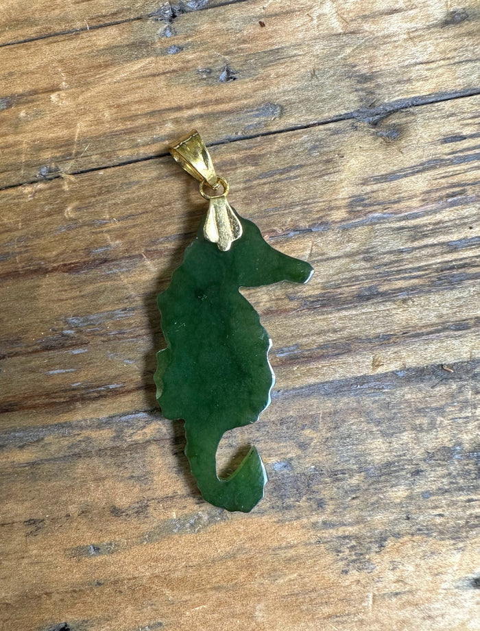 Green jade seahorse pendant with gold bail resting on a wooden surface