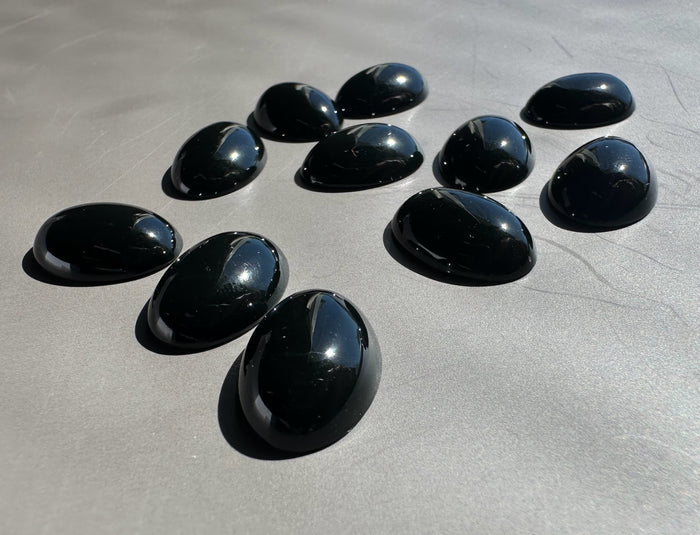Group of glossy black Wyoming Edwards Jade oval cabochons on a metallic surface