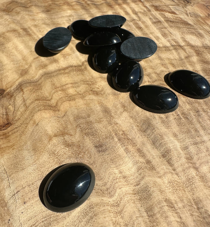 Group of glossy black oval Jade cabochons and flat backing discs spread on a wooden surface