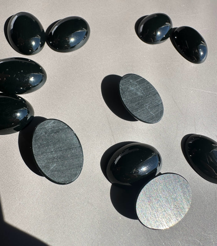 Group of polished jade oval cabochons in deep green on a light gray surface