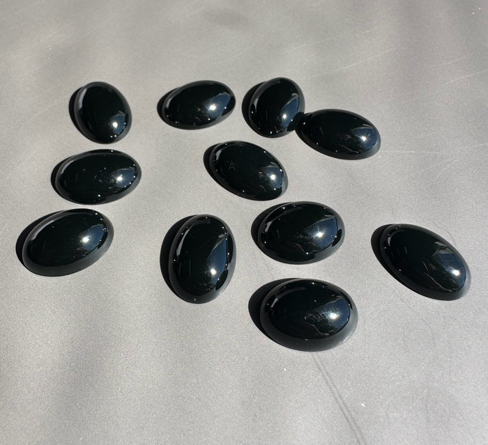 Glossy black oval jade cabochons scattered on a light gray surface.